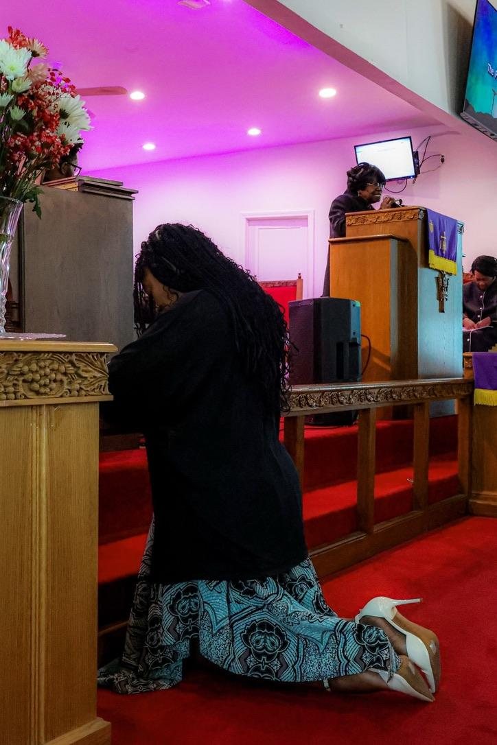 A woman kneeling in prayer at the altar rail beneath the pulpit