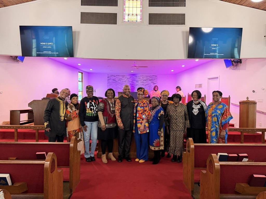Members gathered together at the front of the sanctuary, many dressed in kente and African prints