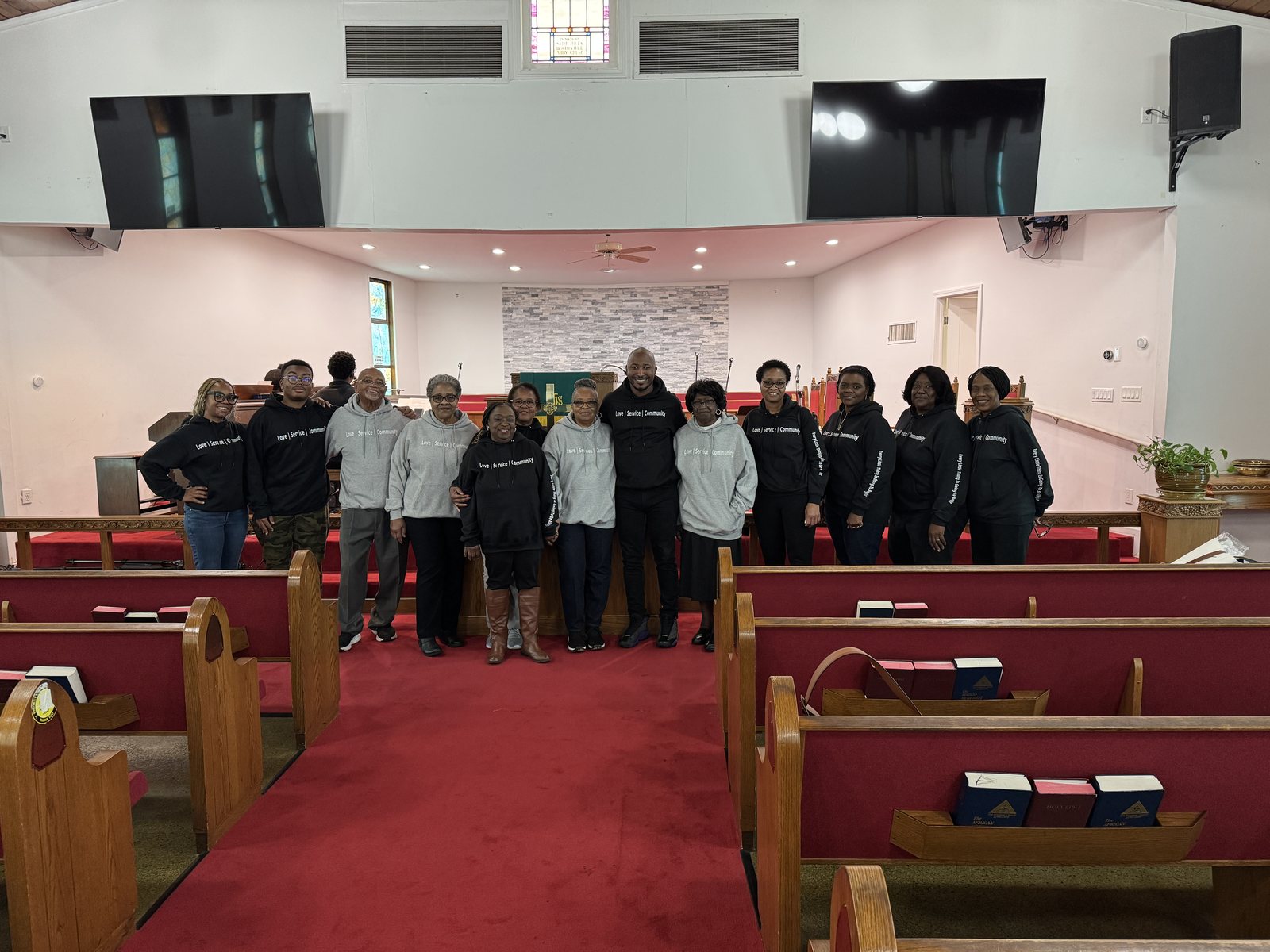 GROW Group Leaders standing together in the sanctuary aisle with the pastor, in Love, Service, Community sweatshirts