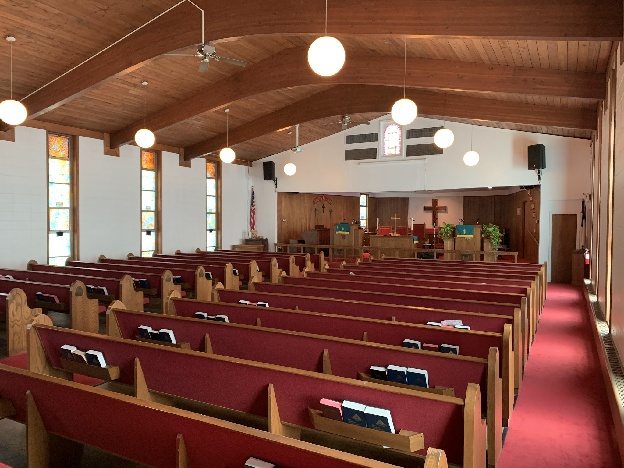 The sanctuary before the renovation, with rows of wooden pews, red cushions and stained-glass windows