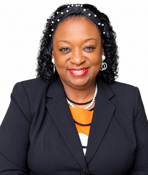 Sister Glenda Davis smiling, in a black blazer with pearl and orange accents