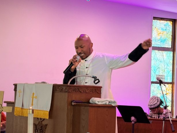 Rev. L. Christopher Lewis preaching at the pulpit, microphone in hand and one arm raised