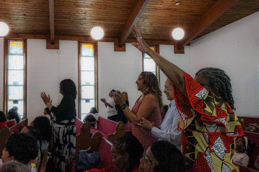 Worshippers standing with hands raised in praise between the pews