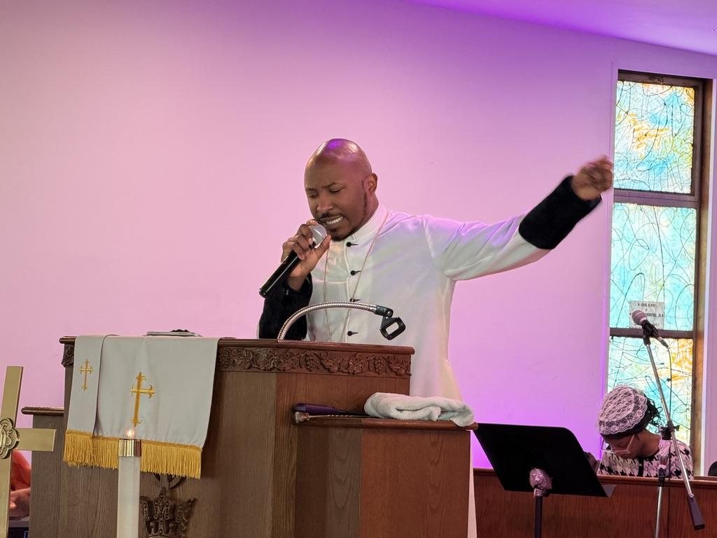 A minister in a white robe preaching from the pulpit with arm outstretched