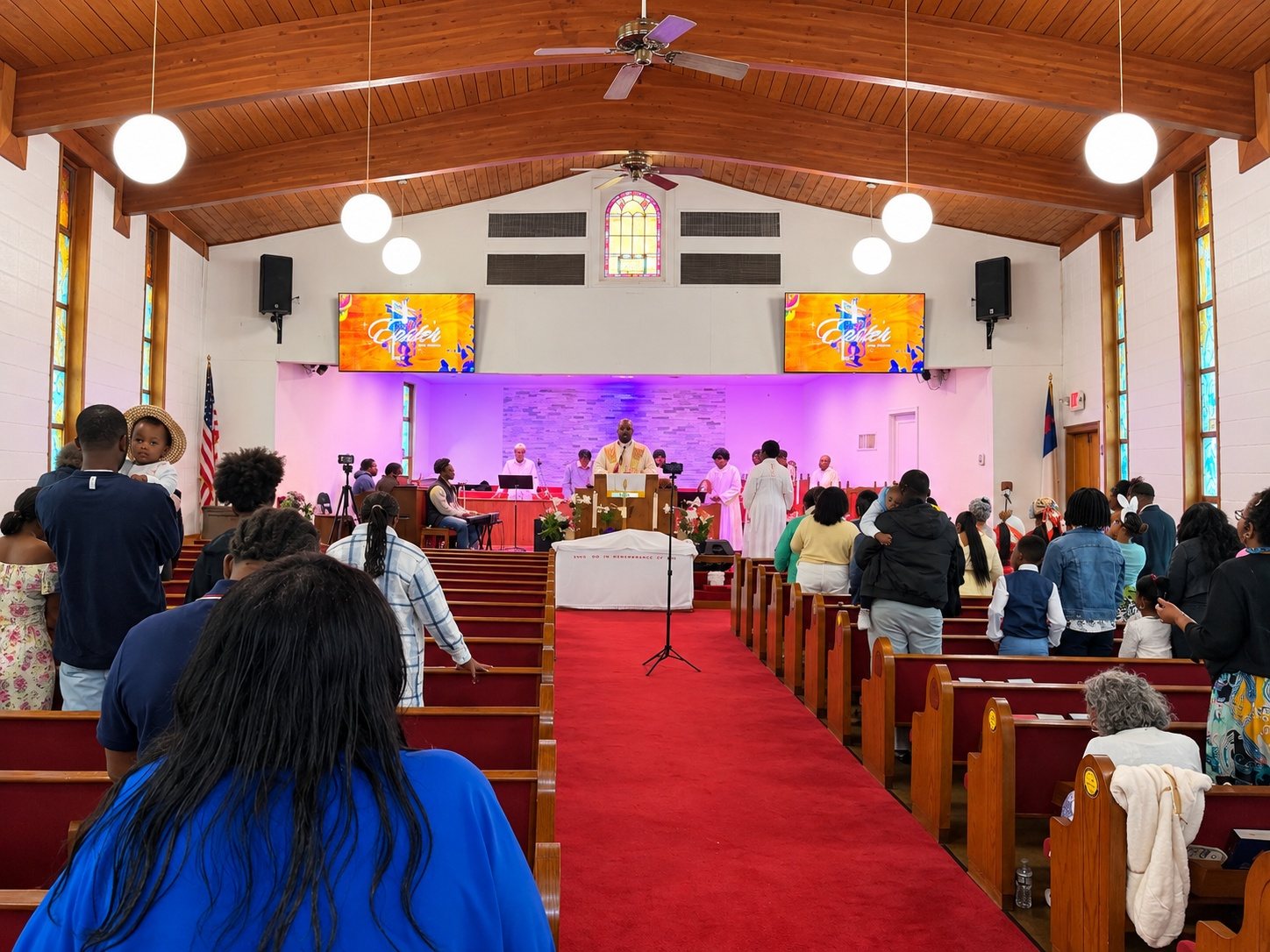 The congregation standing in the pews during worship, facing the pulpit under a purple-lit chancel and two screens