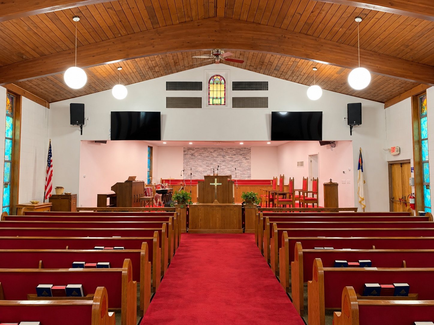 The empty sanctuary looking up the red-carpeted aisle to the pulpit, with wooden pews, a wood-beamed ceiling and two screens
