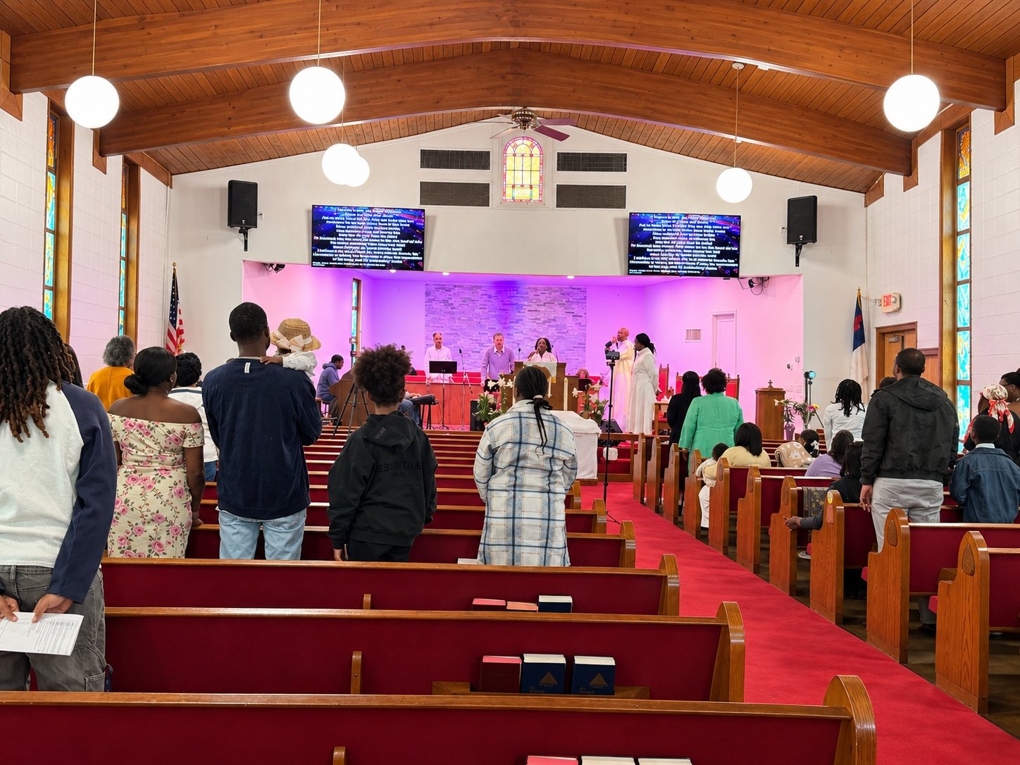 The congregation standing in the red-carpeted sanctuary during worship, facing a purple-lit chancel