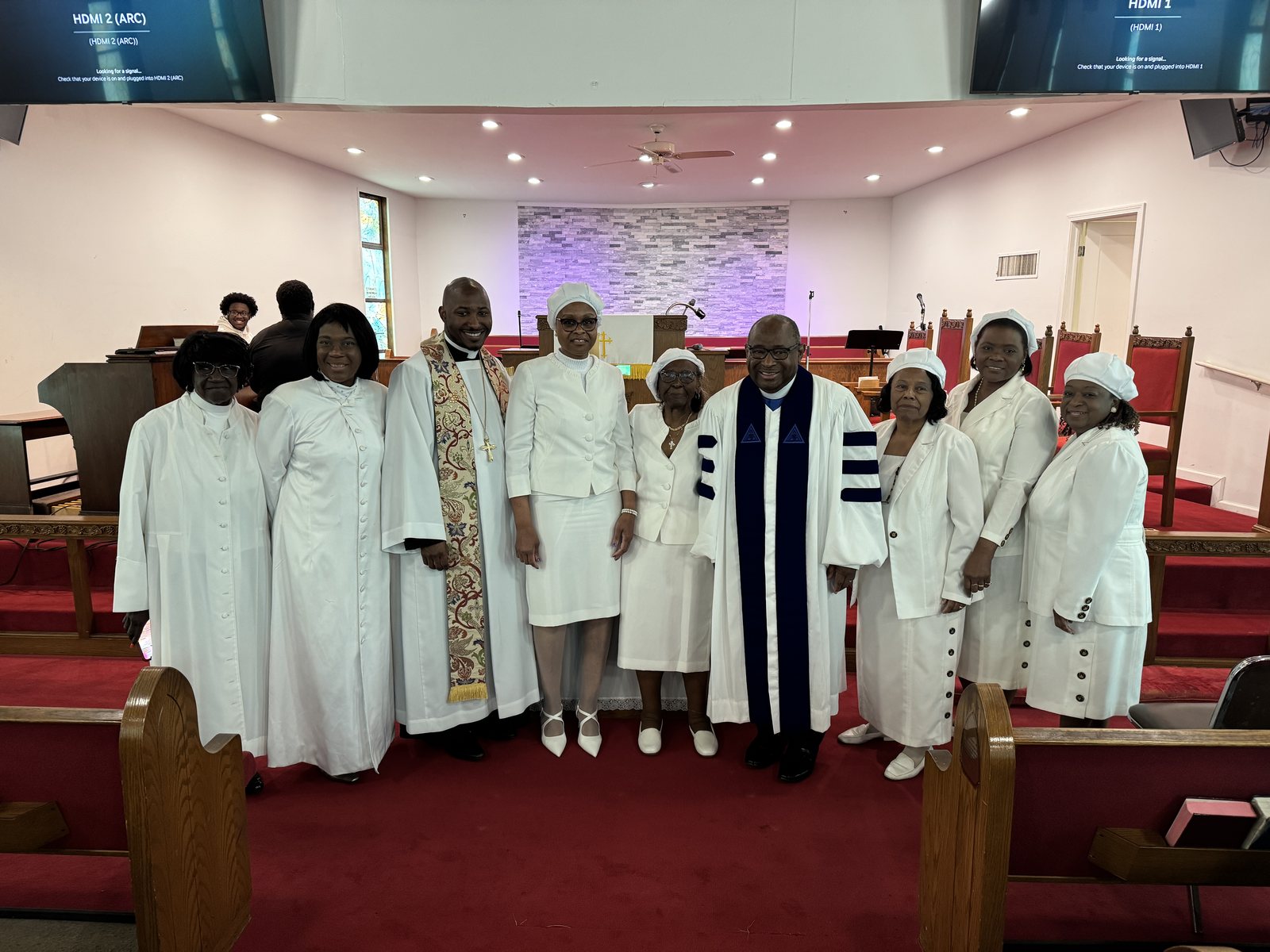 Members of the Women’s Home and Overseas Missionary Society in white with the pastor and a minister at the front of the sanctuary